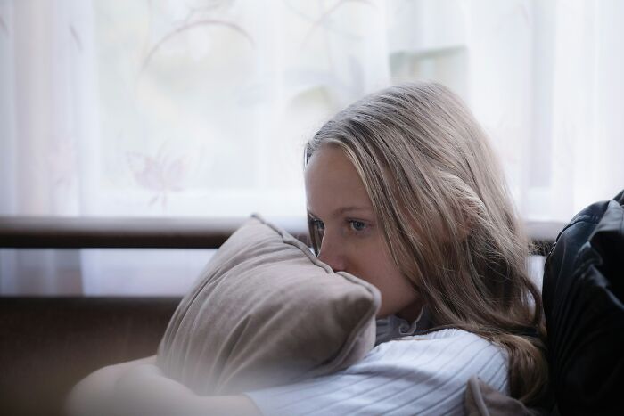 Young woman struggling in life, sitting alone on a couch holding a pillow, showing emotional stress in a relationship.