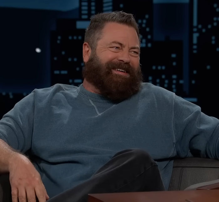 Nick Offerman sitting on a talk show couch, smiling and wearing a blue sweatshirt during an interview. Nick Offerman sitting on a talk show couch, smiling and wearing a blue sweatshirt during an interview.