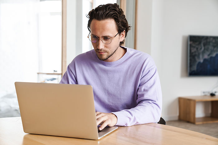 Man in glasses and purple sweater focused on laptop, representing non-profit employee accused of fudging hours. Man in glasses and purple sweater focused on laptop, representing non-profit employee accused of fudging hours.