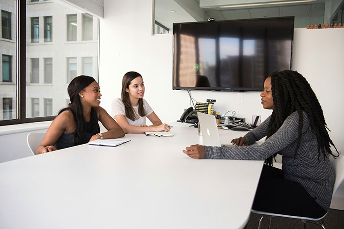 Three women having a discussion in a modern office, illustrating a non-profit employee hours dispute scenario. Three women having a discussion in a modern office, illustrating a non-profit employee hours dispute scenario.