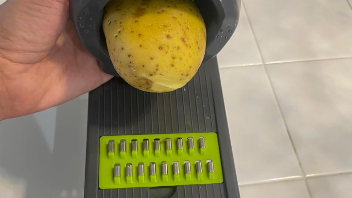 Hand using a multi-tasking kitchen tool to grate a potato, showcasing versatile home gadget functionality.