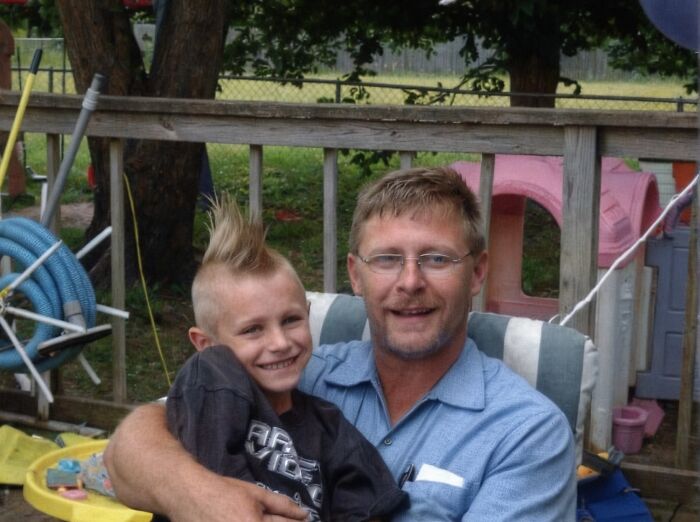 A dad and his son smiling outdoors on a porch, capturing a heartfelt moment related to a late son&rsquo;s heartbeat teddy bear.