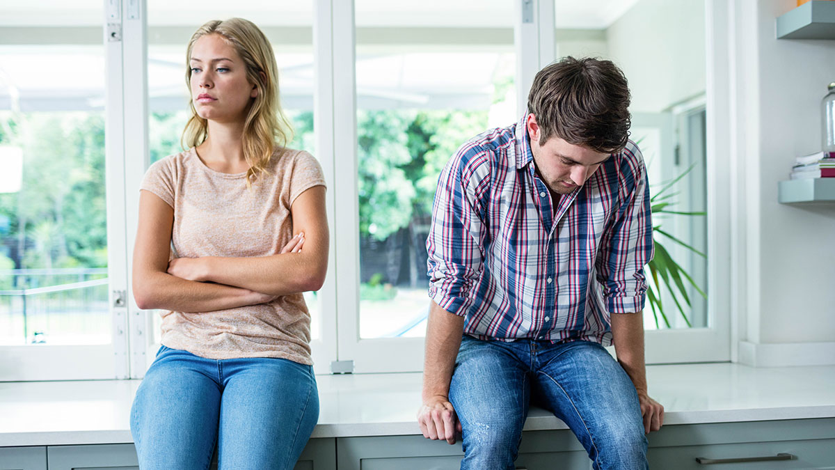 Upset woman and man avoiding eye contact, sitting apart in a bright room after a tense party bathroom incident.