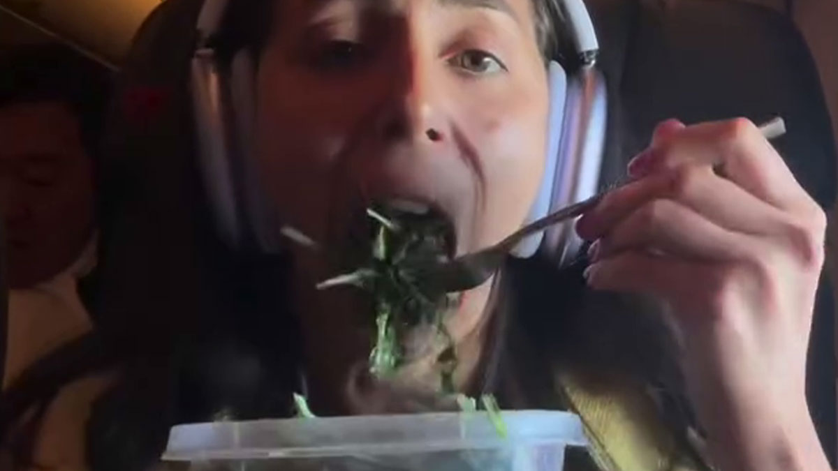 Plane passenger eating homemade salad mid-flight wearing headphones while seated inside an airplane cabin.