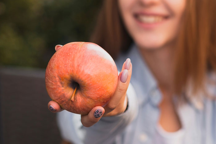 A woman smiling and holding an apple related to K9 sniffing undeclared fruit in passenger luggage. A woman smiling and holding an apple related to K9 sniffing undeclared fruit in passenger luggage.