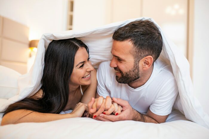 Couple smiling and holding hands under a blanket, highlighting themes of insecurity and relationship trust issues.