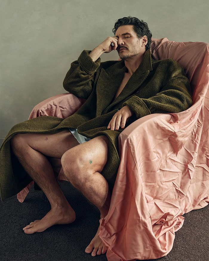Pedro Pascal seated in a green coat on a pink satin-covered chair, appearing contemplative. Pedro Pascal seated in a green coat on a pink satin-covered chair, appearing contemplative.