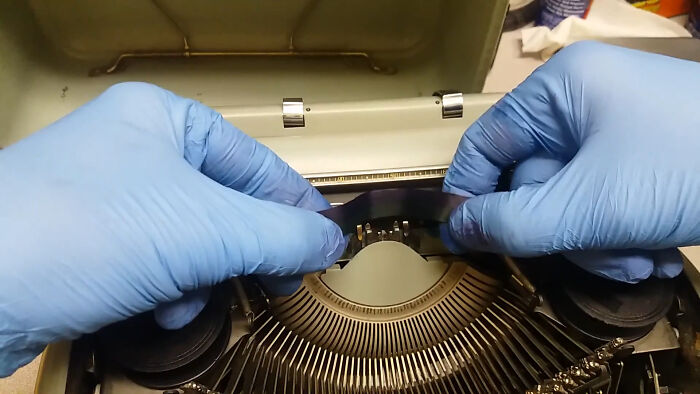 Hands wearing blue gloves installing a typewriter ribbon, showcasing a skill people online needed before the 2000s.