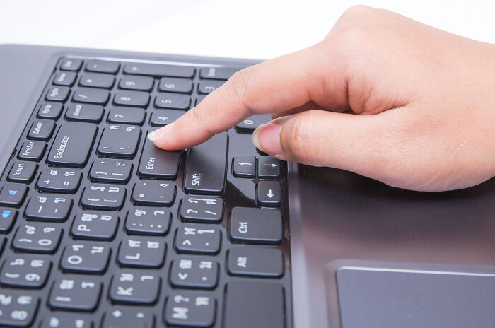 Close-up of a hand pressing the enter key on a laptop keyboard, illustrating skills people online needed before the 2000s.