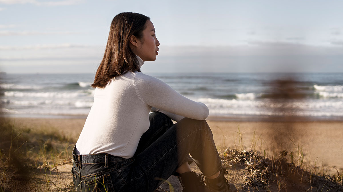 Young woman sitting and reflecting by the beach, symbolizing skills people online needed before the 2000s now obsolete.