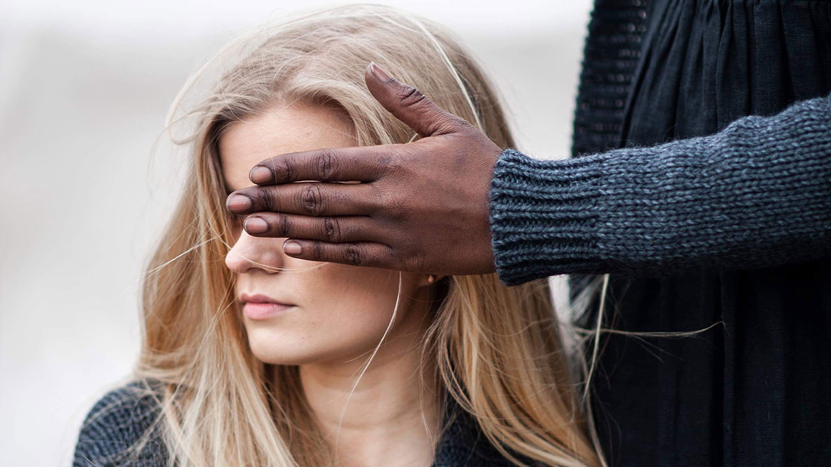 A person covering a woman's eyes with their hand, illustrating big no no to do in your country concept.