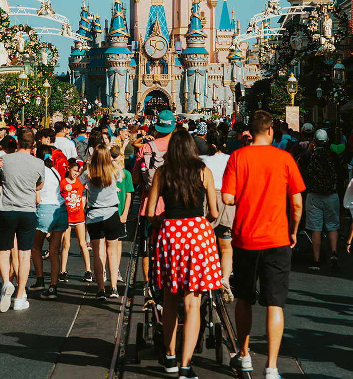 Crowd walking toward Disney castle with woman in red polka dot skirt amid debate over inappropriate outfit complaint. Crowd walking toward Disney castle with woman in red polka dot skirt amid debate over inappropriate outfit complaint.