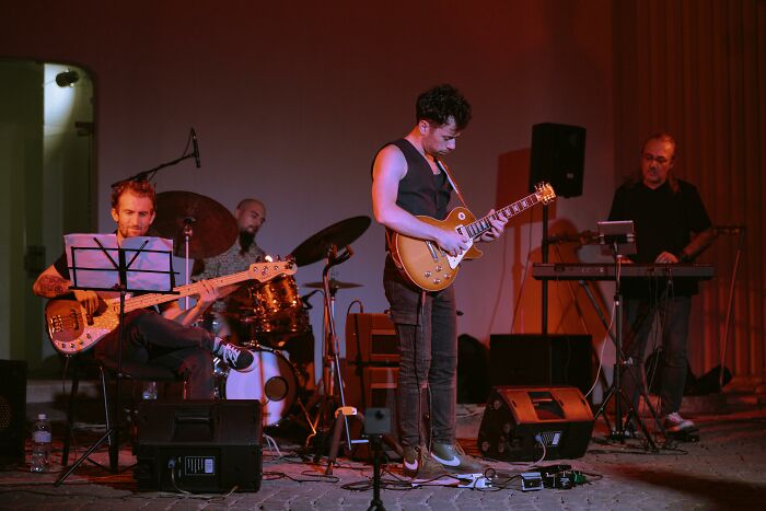 Band performing live on stage with guitar, bass, drums, and keyboard highlighting professions and awful people theme.