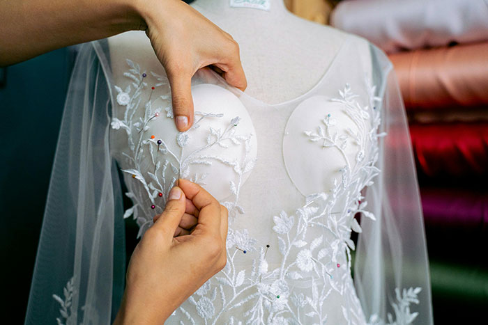 Hands adjusting embroidery on a white wedding dress, highlighting intricate floral details for wedding dress sisters drama. Hands adjusting embroidery on a white wedding dress, highlighting intricate floral details for wedding dress sisters drama.