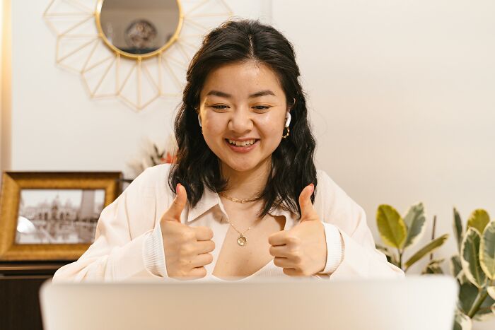 Young woman showing thumbs up during an online video call, illustrating subtle signs of low self-esteem.