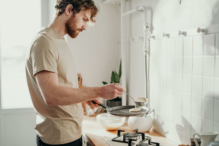 Young man cooking breakfast in a bright kitchen.