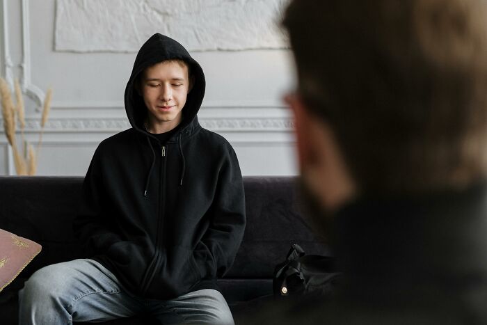 Teenager in a black hoodie sitting with eyes closed, reflecting on one wrong deed that changed life forever.