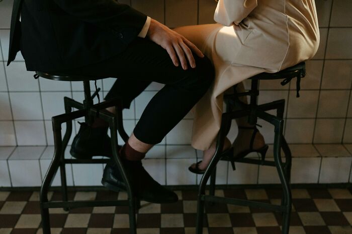 Two people sitting on stools at a bar, one touching the other's knee during a date that went so sour safe word was used.