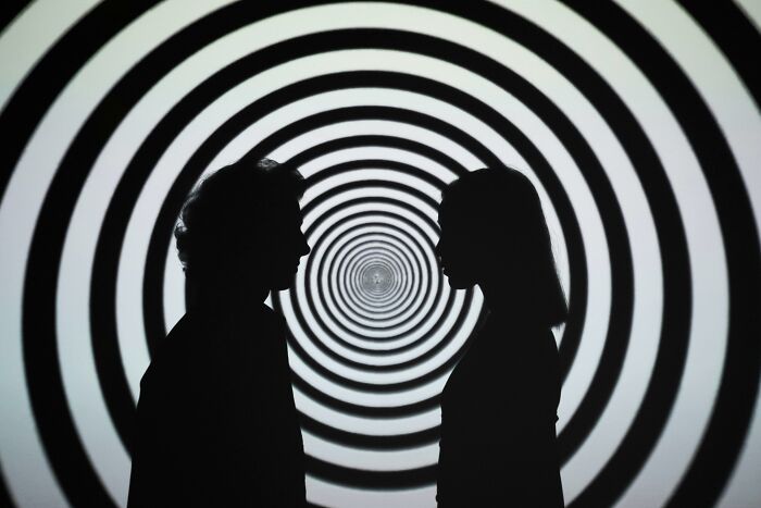 Silhouettes of two people facing each other against a hypnotic spiral pattern symbolizing theories about the afterlife.