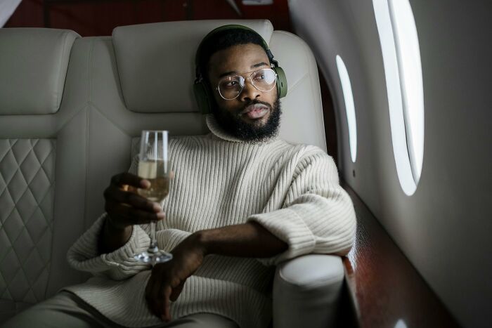 Man wearing glasses and headphones, relaxing with a drink on a private jet, illustrating privileged things said.