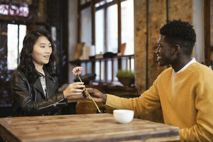 A young man and woman sharing a flower during a date.