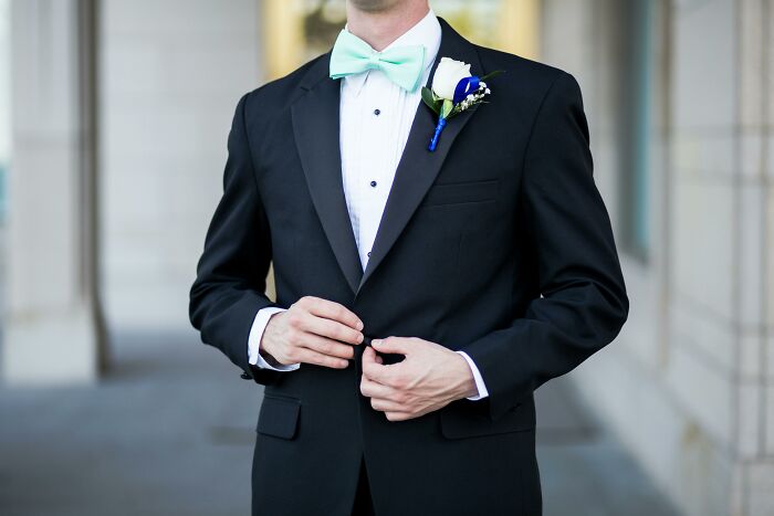 Man in a black tuxedo adjusting jacket, wearing mint bow tie and boutonniere, illustrating privileged things shared by people