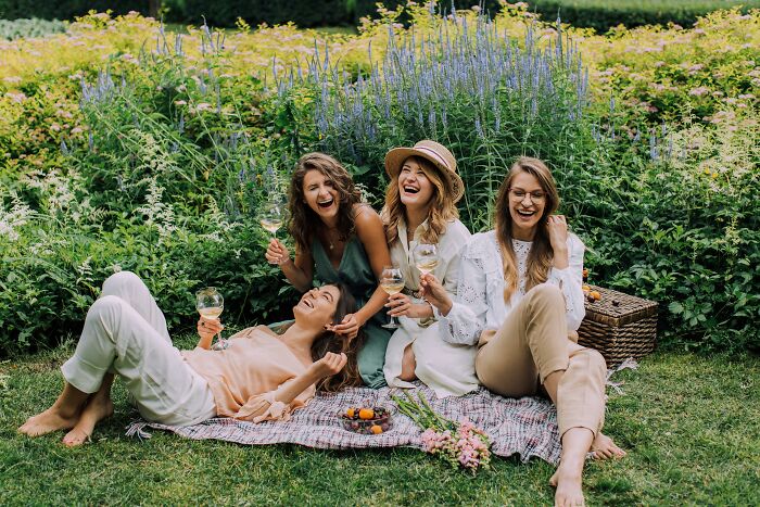 Four women enjoying a garden picnic, sharing laughs and wine.