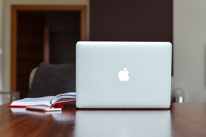 Silver Apple laptop on a wooden table with an open notebook and smartphone, illustrating people share privileged things said.
