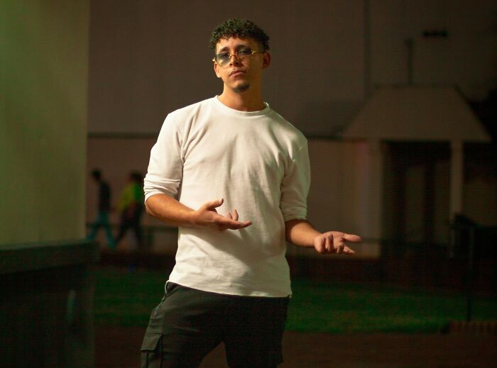 Young man in casual white top and glasses gesturing outdoors at night representing people sharing most privileged things said.
