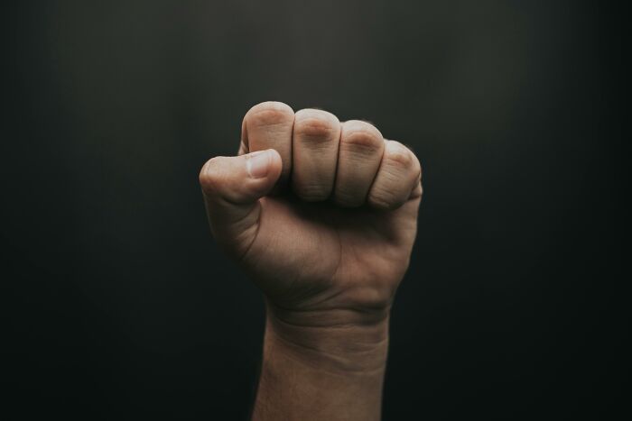 Fist clenched in front of dark background symbolizing strength and confrontation in coworker diabolical things report HR.