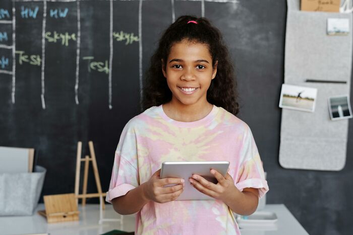Girl holding tablet and smiling in front of a chalkboard showing adults who never moved on from their glory days in high school.