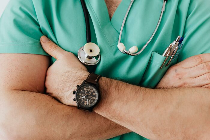Close-up of a person in green scrubs with arms crossed wearing a stethoscope, symbolizing coworker diabolical things report HR.