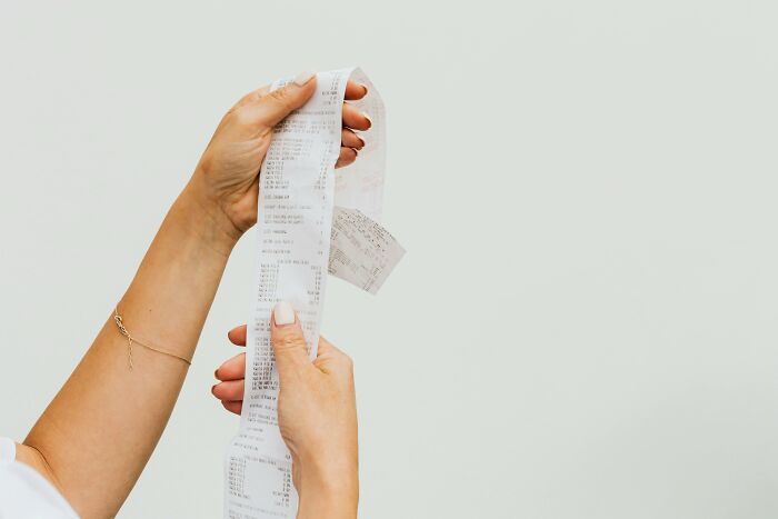 Person holding and examining a long receipt, illustrating a relatable middle class moment of budgeting and expenses.