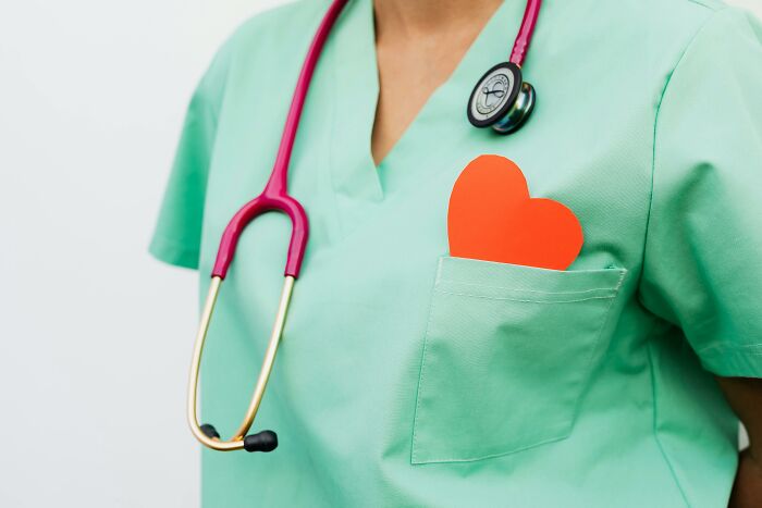 Healthcare worker in green scrubs with red paper heart in pocket and stethoscope, representing coworker diabolical things report HR.