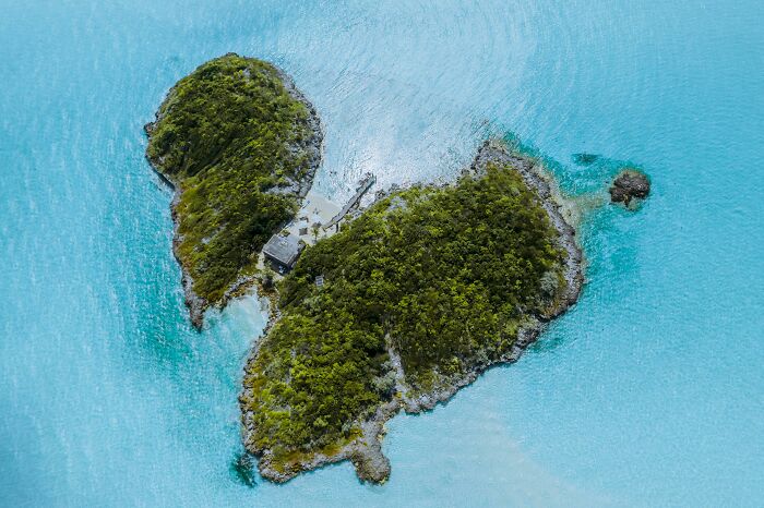 Aerial view of a lush private island surrounded by clear blue water, symbolizing privileged things shared by people.