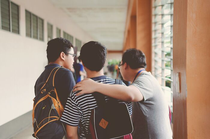 Three adults showing high school nostalgia, walking in a school hallway with backpacks and casual clothing.