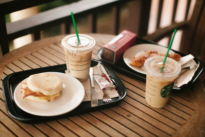 Iced coffee drinks with breakfast sandwiches and pastries on a wooden table, showing relatable middle class flags.