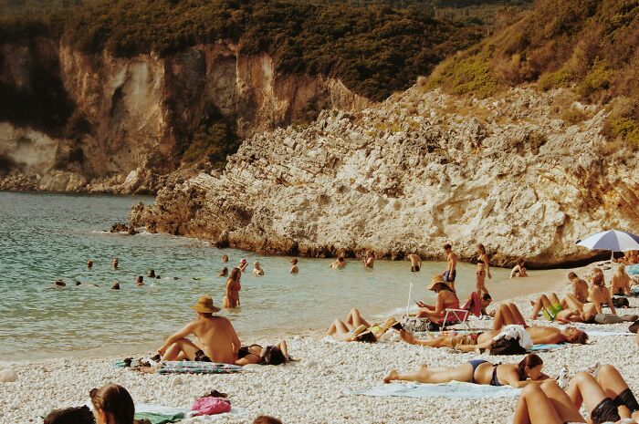 People relaxing and swimming at a sunny beach, sharing moments of privileged leisure and enjoyment by the rocky shore.