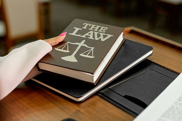 Hand holding a law book with scales of justice symbol.