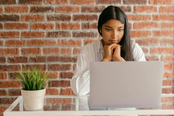 Woman reflecting deeply while using laptop, portraying feelings of cultural outsider and raising children alone.