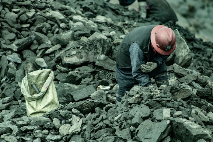 Worker wearing a hard hat sorting rocks in a rugged outdoor setting representing tough professions attracting awful people.