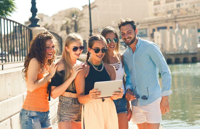 A group of young people smiling and looking at a tablet outdoors.