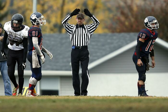 Adult football players on field with referee signaling touchdown, showing they never moved on from their glory days.