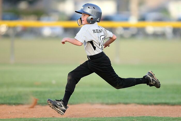 Young boy in baseball gear running on field, showing adults who never moved on from their high school glory days.