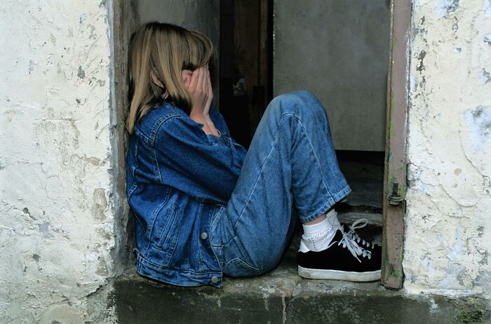 Teenager sitting on a step against a wall, covering face, illustrating adults who never moved on from their high school glory days.