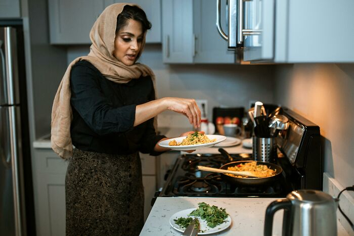 Woman wearing a headscarf cooking in kitchen, representing wife adopting husband’s culture while raising three kids alone.