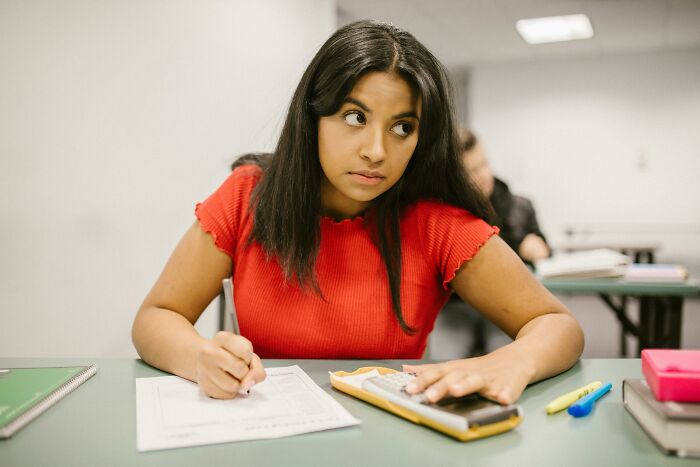 Teen girl in red shirt solving math problems using a calculator, focused on a high school math quiz. Teen girl in red shirt solving math problems using a calculator, focused on a high school math quiz.