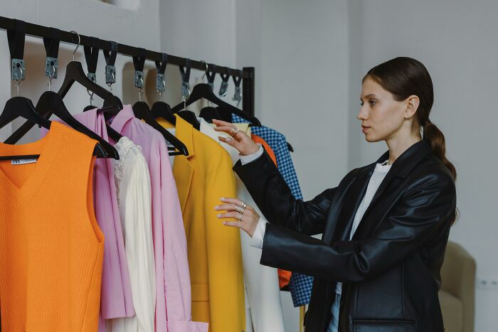 Woman in black leather jacket choosing clothes from a rack with colorful garments, people share most privileged things said.