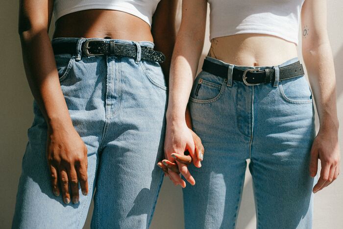 Two people wearing jeans and crop tops holding hands closely, showing commitment and connection.