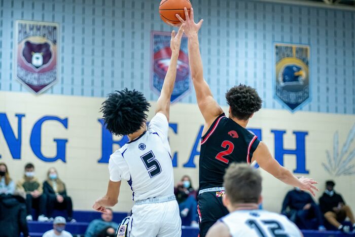 Two high school basketball players jumping to reach the ball during a game showing adults stuck in glory days.